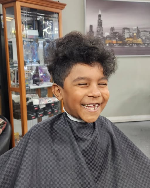 A smiling young client in the barber chair at Medina’s